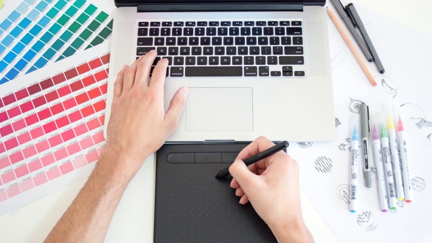 A person typing on a laptop and drawing on a tablet.