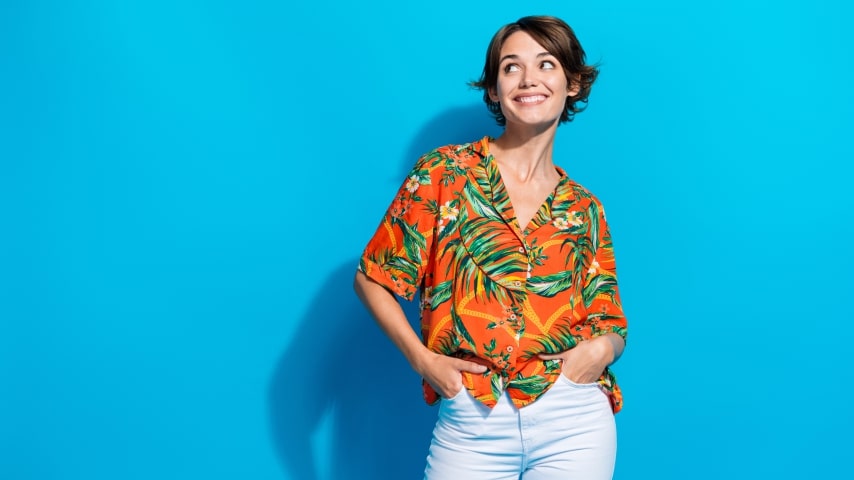 A woman wearing a colorful orange AOP shirt with a pattern of leaves and flowers.