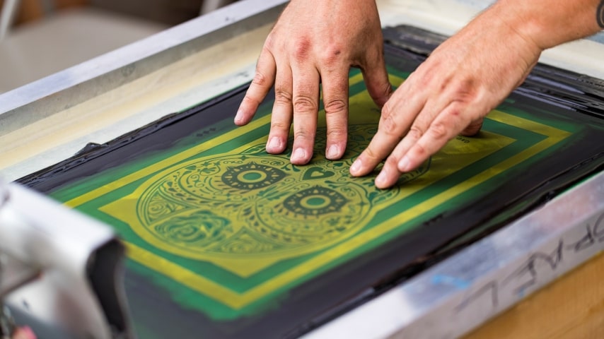A person using screen printing equipment to make a custom t-shirt.