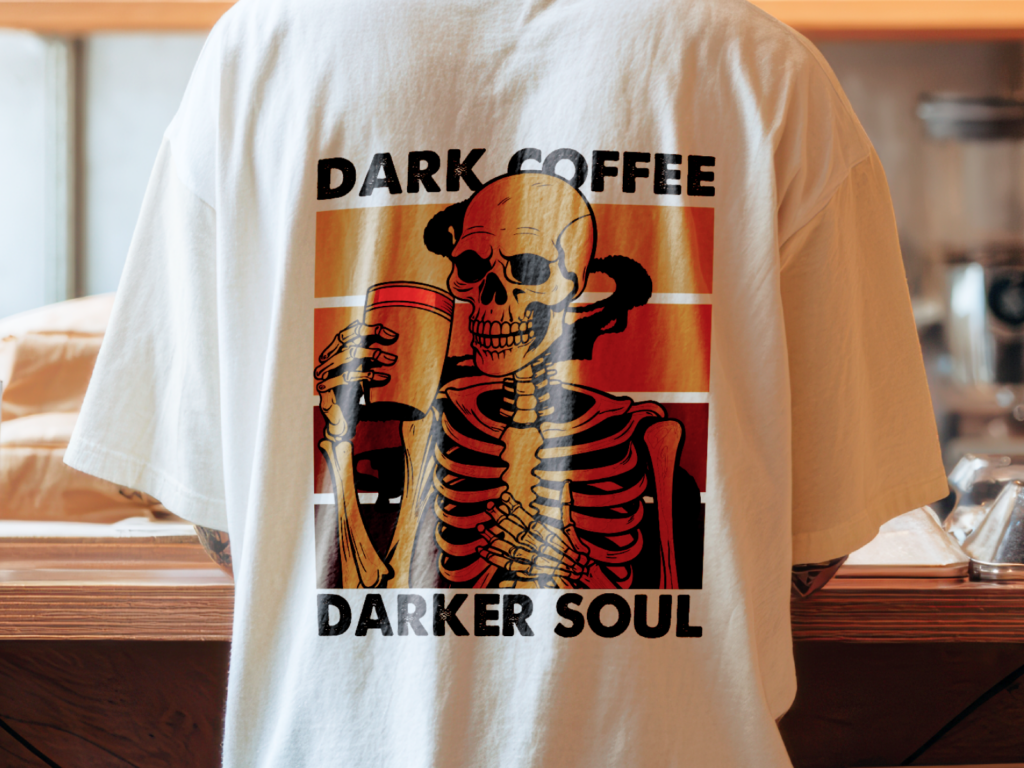 Back of a white t-shirt showing a skeleton holding a coffee cup, with the text "Dark Coffee, Darker Soul" in bold black letters.