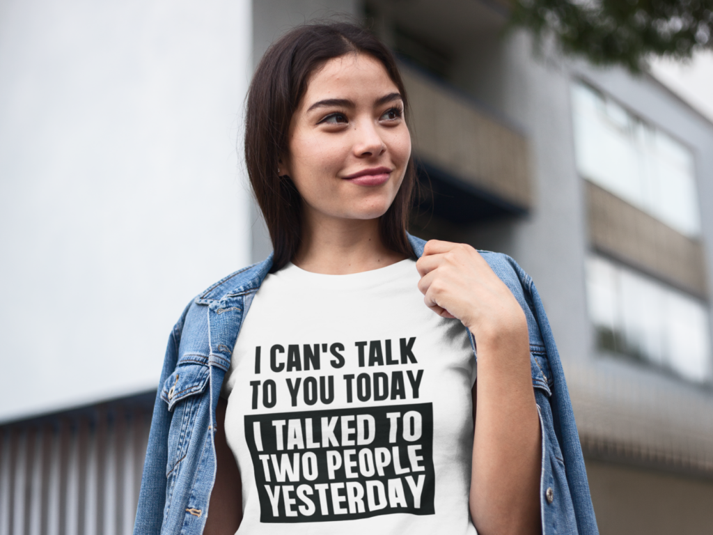 Woman outdoors, smiling and wearing a denim jacket over a white "I can't talk to you today, I talked to two people yesterday" tee.