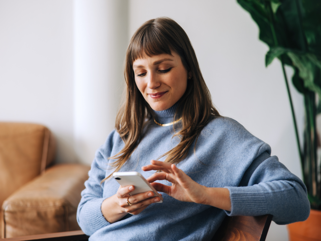 A woman sits comfortably on a chair, scrolling through her phone.