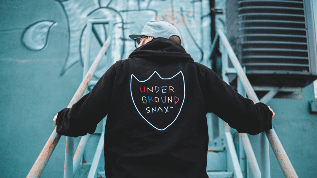 A young man in a black hoodie with “Underground snax” embroidered on the back of the hoodie.