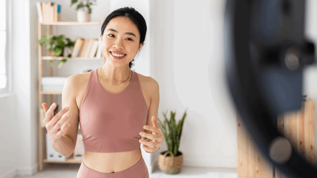 A smiling woman dressed in athletic apparel is recording herself using a mobile phone.