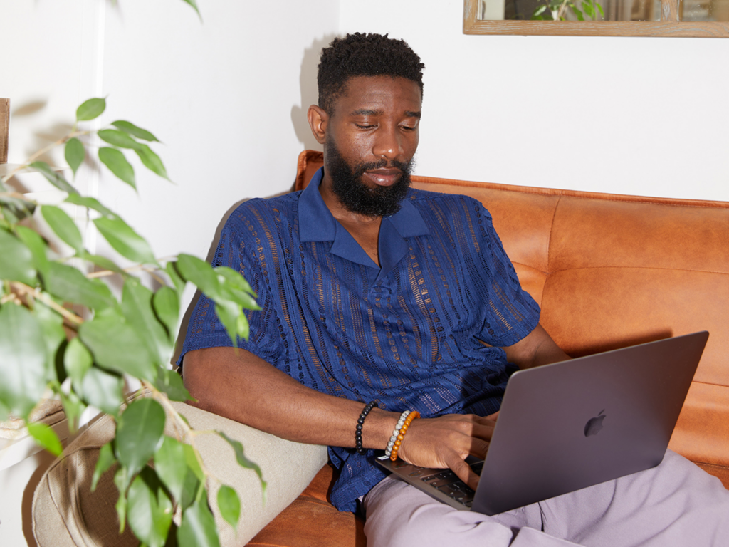 A man sits on a couch with a laptop, focused on optimizing his online store.