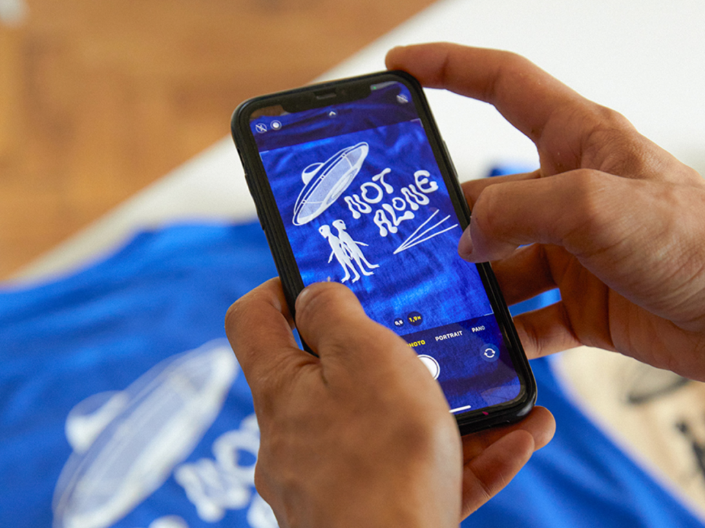 A person taking a picture of a custom blue “Not Alone” t-shirt using a mobile phone.