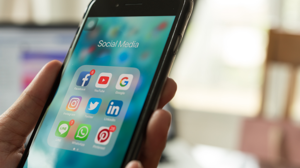 A person holding a mobile phone with various social media app icons on display.