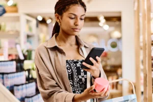 A woman holding a shopping bag while looking at her phone, appearing engaged in a conversation or shopping online.